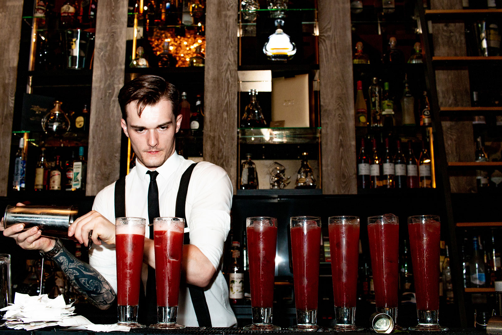 Barman pouring seven red cocktails on bar
